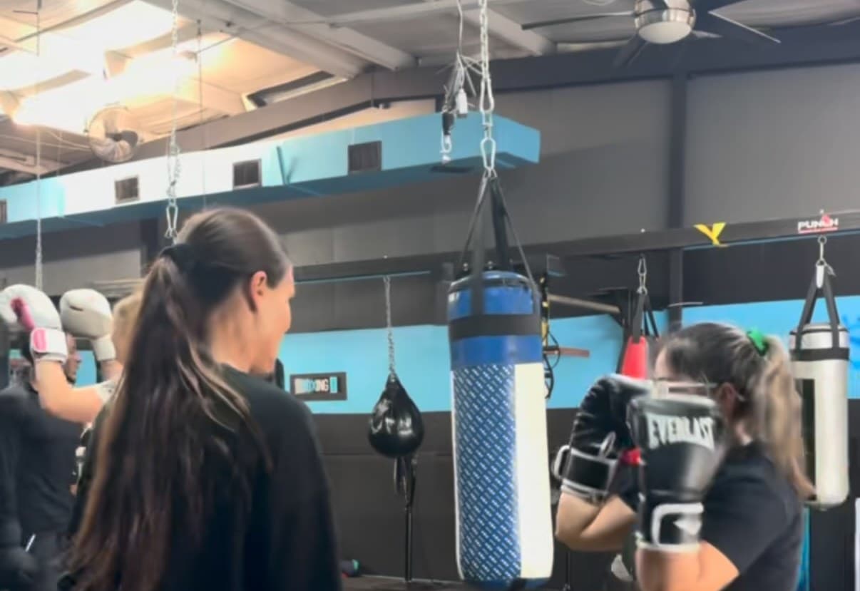 The main gym floor, with the row of hanging heavy bags and a coach on the mitts